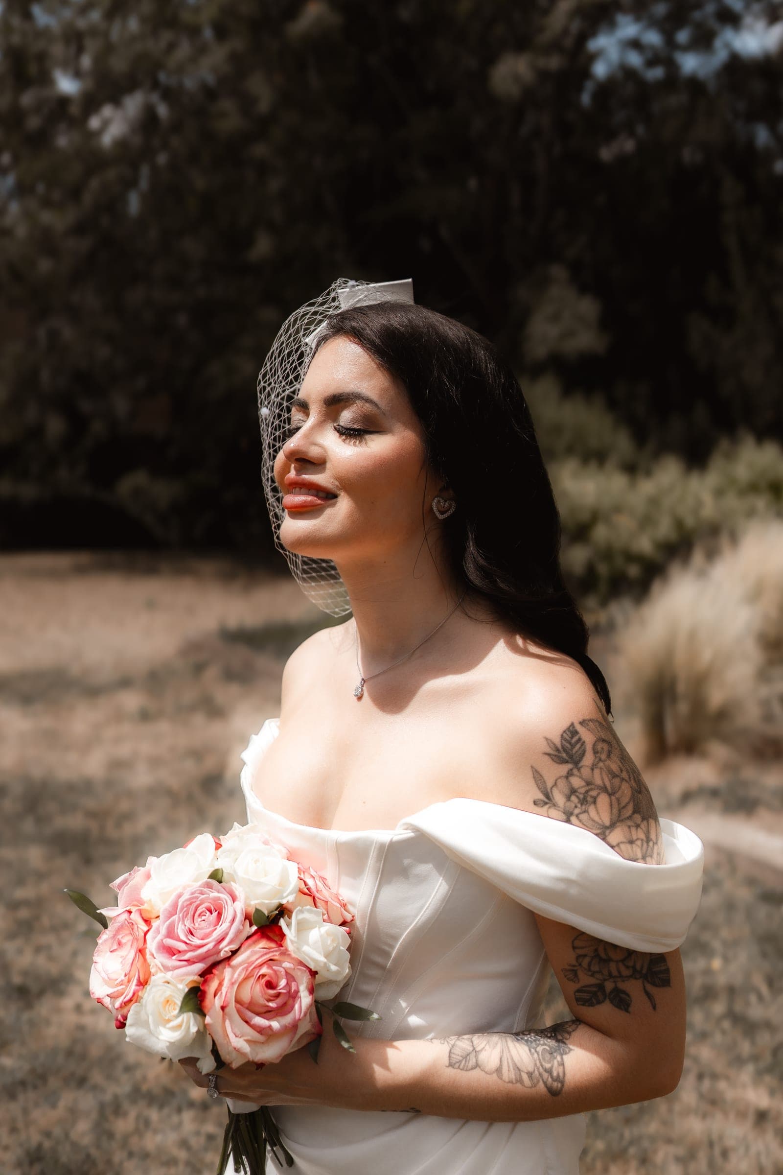 A sunlit bride holding a pink and white rose bouquet among golden meadow grasses at Cheshunt Register Office