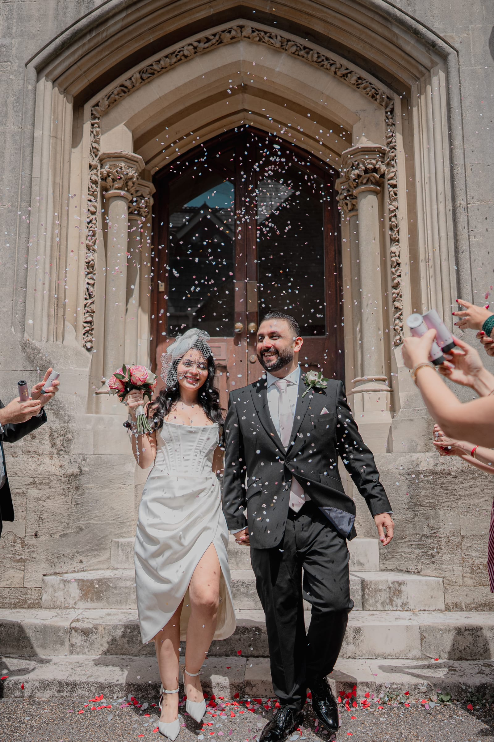 A confetti throw for a couple leaving through the stone Gothic arch at Cheshunt Register Office