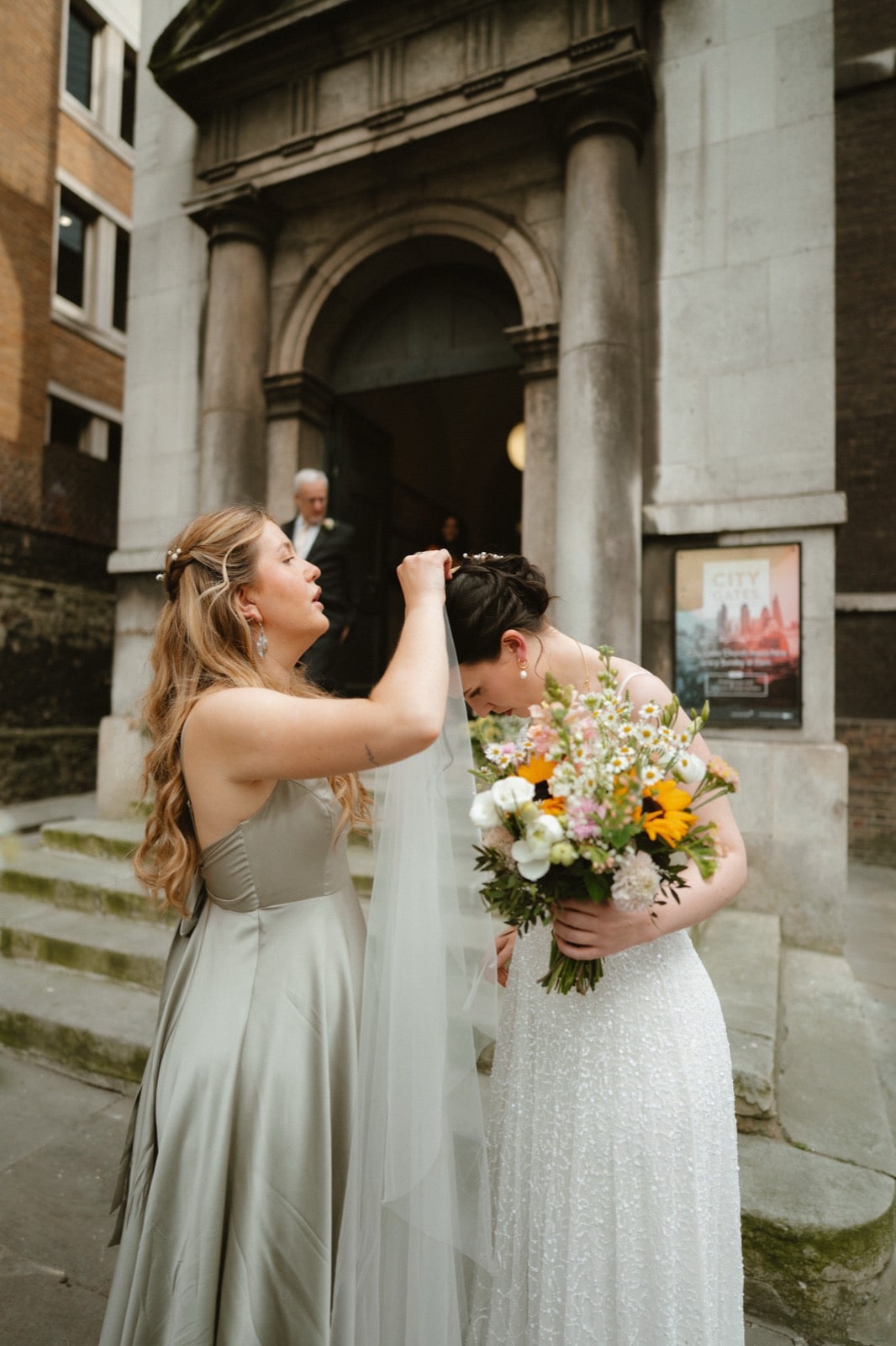 Bride having her veil adjusted outside All Hallows-on-the-Wall church, City of London