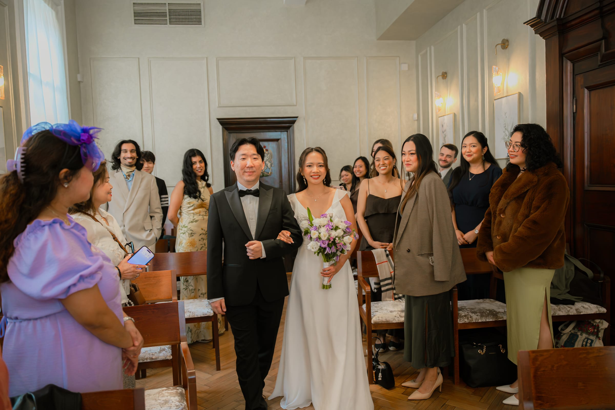 A bride entering on her father’s arm through standing guests at a London register office ceremony