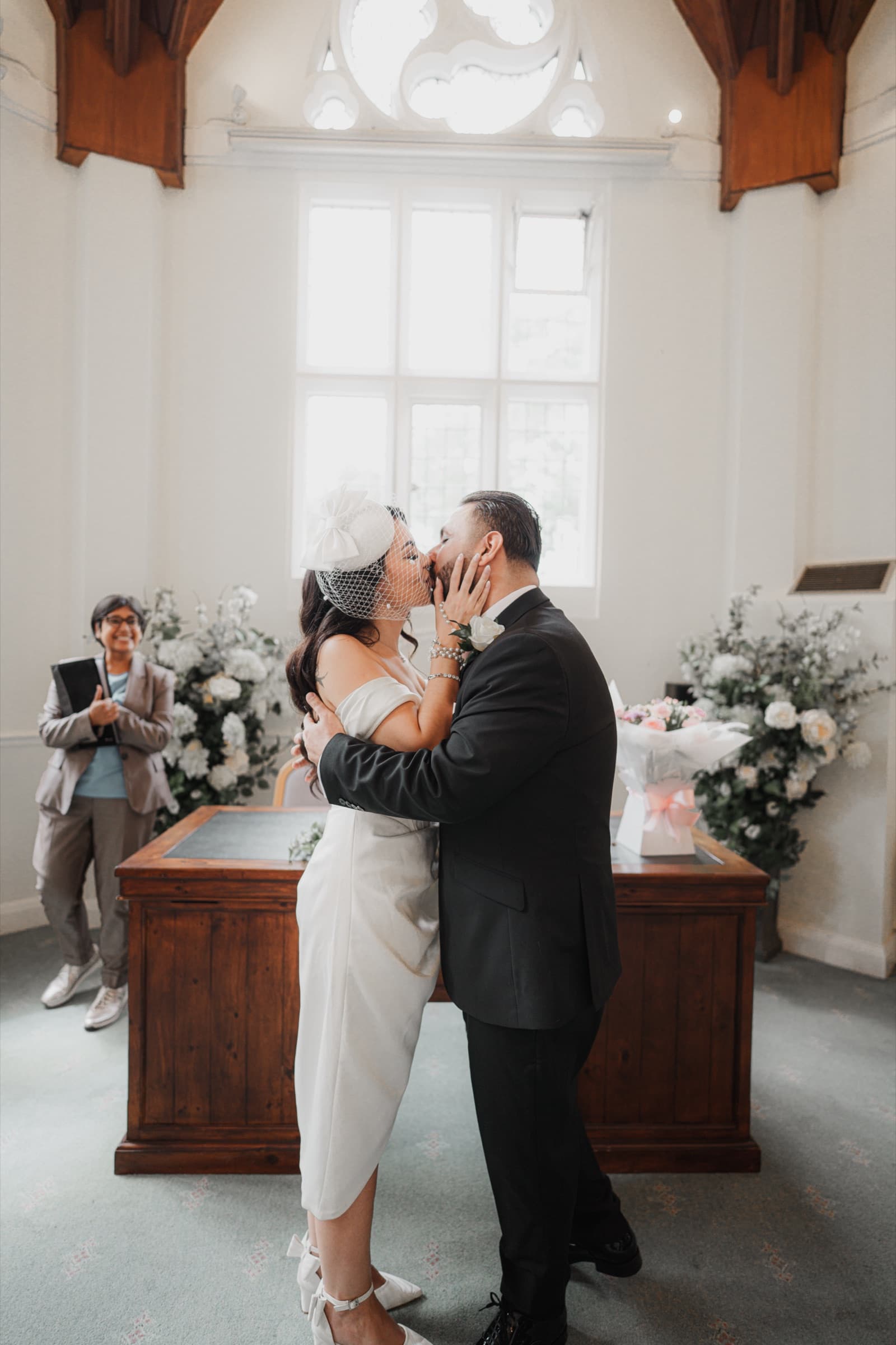 A couple’s first kiss as the registrar looks on at a London register office wedding, photographed by Evocation Photography