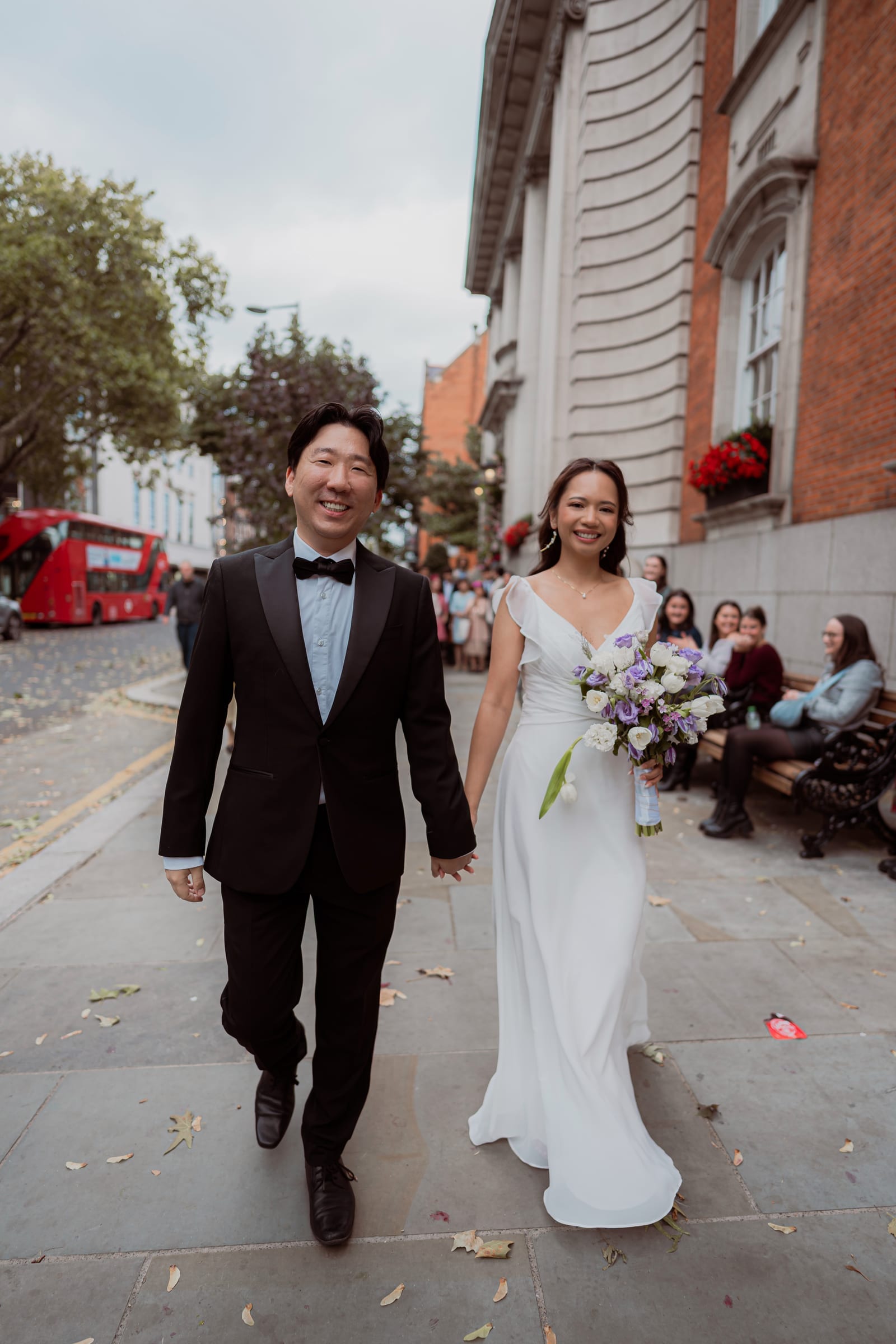 A newly married couple walking past a London town hall with a red bus behind them
