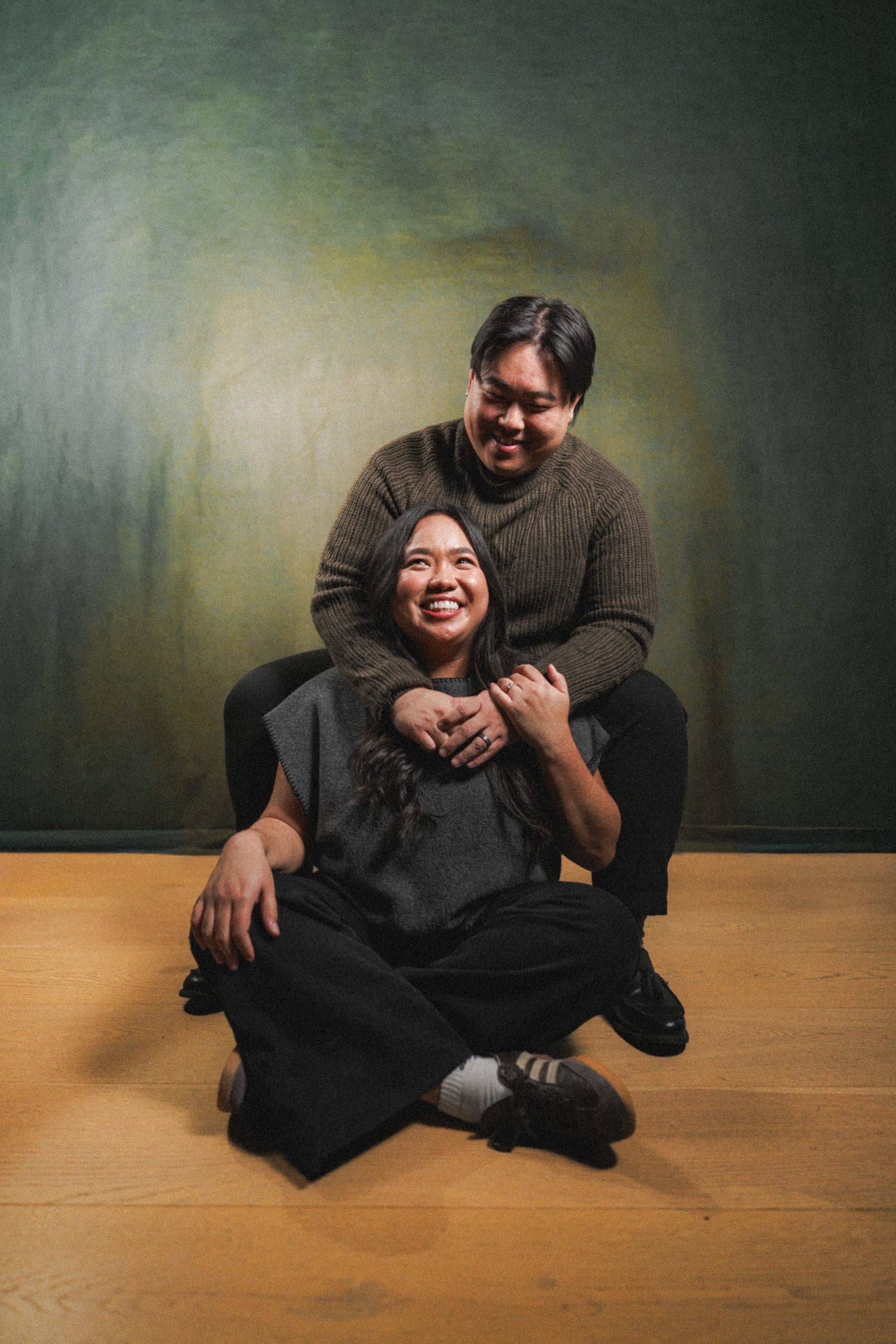A laughing couple in a relaxed studio portrait against a deep green backdrop