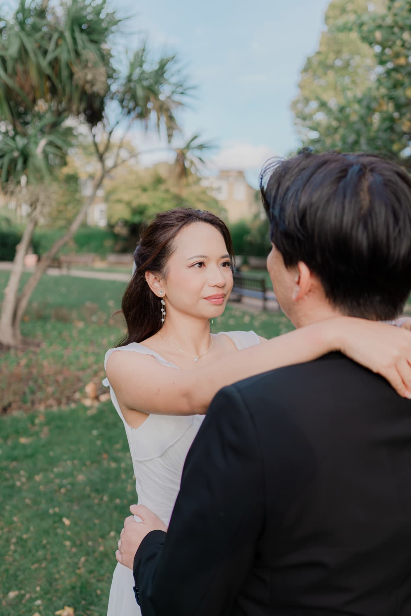 Bride with her arms draped around the groom’s neck, gazing at him with a serene expression in soft warm light